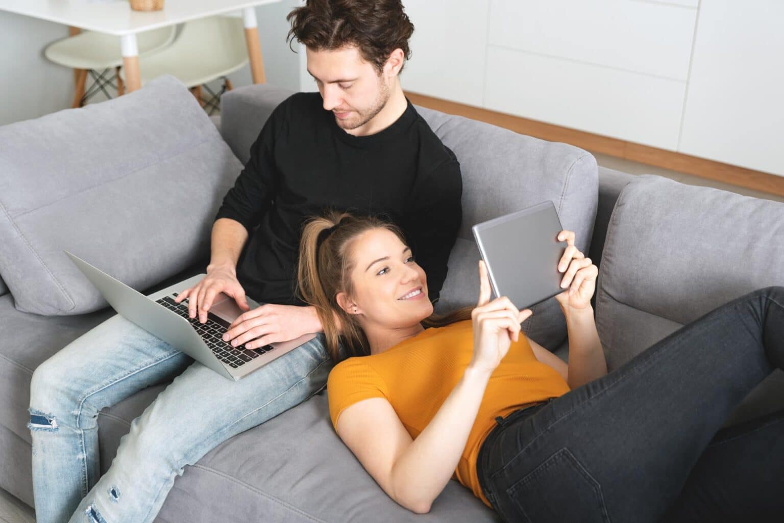 Ein Paar, das auf der Couch sitzt und mit Laptop und Tablet im Internet surft